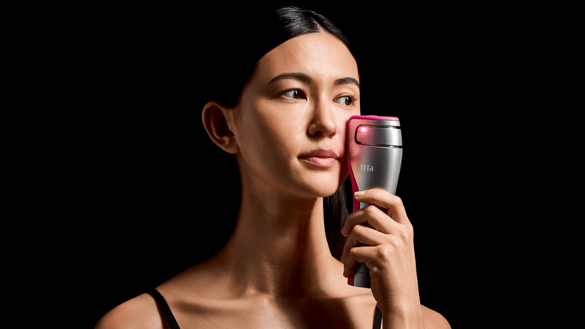 Woman using Tria FRX laser on skin texture pictured on a black background